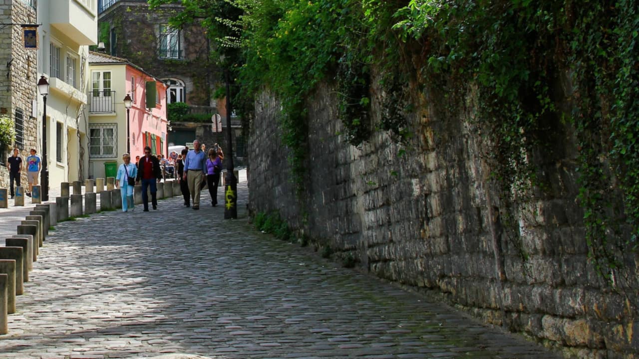 Une ruelle pavée de Montmartre, entre un mur de pierre et des façades colorées